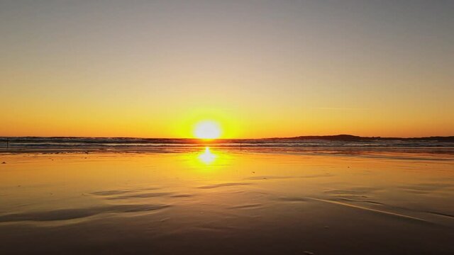 Traveling forward on the Lanzada beach at the edge of the sea during a beautiful sunset with a silhouetted fisherman in Galicia (Spain)