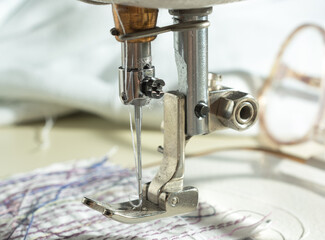 close-up of mechanism with a needle of an electric sewing machine. against the background of glasses and fabric with threads