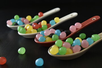 Gros plan sur des cuillères alignées sur fond noir et remplies de bonbons très colorées