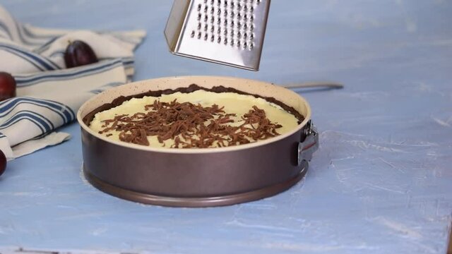 Woman chef holds metal grater and grates chocolate dough. Making chocolate pie.