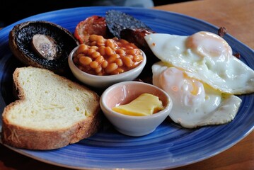 Full English breakfast with a slice of bacon, fried eggs, black pudding, baked beans, butter, mushrooms and toast, served in Newcastle, UK