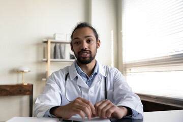 Empathetic young mixed raced doctor giving online help, medical support, therapy advice, consultation. Head shot portrait of male general practitioner looking, speaking at camera. Video call screen - obrazy, fototapety, plakaty