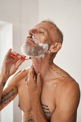 Mature fit man shaving his beard with razor