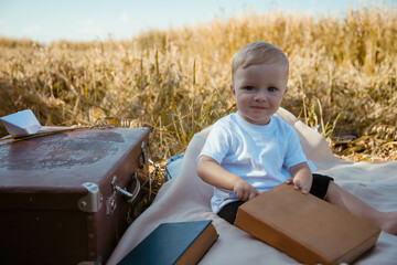 A cute baby girl sits on a blanket with books and an old suitcase. Boy in the summer in the village.