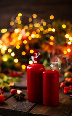 There are red candles on the wooden table. Smoke is coming from the newly extinguished wicks.