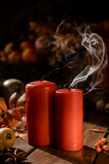 There are red candles on the wooden table. Smoke is coming from the newly extinguished wicks.
