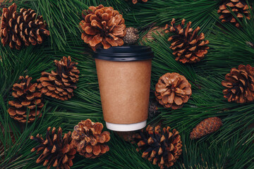 Green pine tree branches, cones background, paper cup of coffee mock up, top view. Merry Christmas beverage, hot drink for winter walk, social distancing, self-care, covid-19 concept