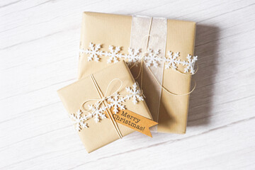 Christmas presents on white wooden background. Natural winter theme decoration, brown paper, twine, snowflake ribbon, tag. Selective focus. Sustainable gift wrapping. Gift giving. Merry Christmas.