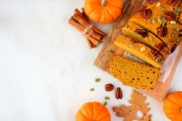 Autumn pumpkin bread sliced. Above view table scene over a white marble background. Copy space.