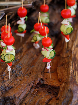 Healthy salad with vegetables tomatoes, cucumbers and greens on small sticks for picnic. Close up, selective focus, side view