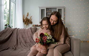 a little daughter and her mother are sitting on the sofa with a bouquet of flowers