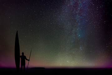 Silhouette of a man with a sea kayak and a double-bladed paddle, marvelling at the night over Lake Superior, Upper Peninsula, Michigan, with the stars of our galaxy as backdrop.