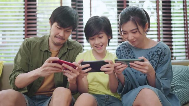 family quality time,asian parent and son sit relax playing game console or smart together laugh joyful smiling on sofa couch in living room at home,asian family homs isolation quarantine ideas concept