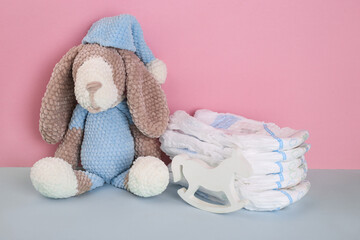 Baby diapers stack cute toy dog sitting on top on blue- pink color background. Newborn nappies concept - obrazy, fototapety, plakaty