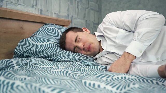 a man in a white shirt lies tired on the bed