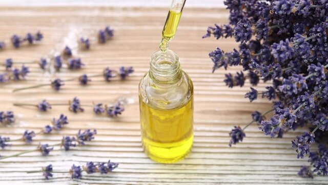 Cosmetic pipette with organic oil. Oil drops fall in the bottle with lavender flowers at the background. Natural skincare and body treatment