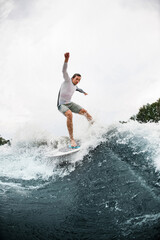 Active healthy man balancing on wave on wakesurf board.