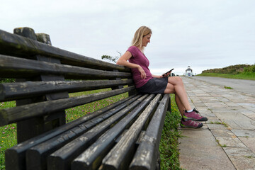 Woman in sneakers sitting on a bench looking at the mobile phone.