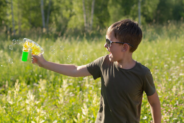 A happy boy with a soap gun in his hands in nature. The emotions of a child