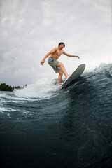 handsome man on wakesurf board and riding river wave on summer day