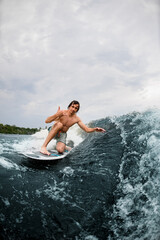 Active man show hand gesture riding the wave on surf style wakeboard