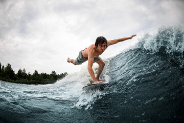 Fototapeta premium man make trick balancing on wake surf board on wave with stretching his leg and hand