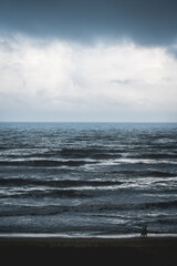 Couple walking on beach along stormy dark silver shining ocean in Daimus, Spain