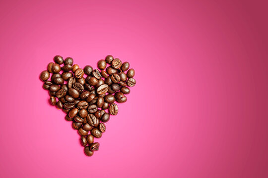 Heart of coffee beans on pink background.