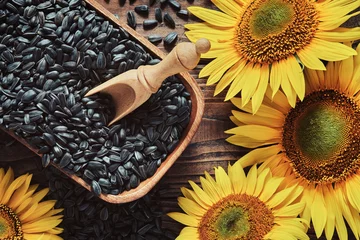 Rolgordijnen Wooden bowl of black sunflower seeds, beautiful yellow sunflowers on wooden board, top view, flat lay. © chamillew