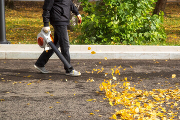 A man, a utility worker, removes leaves from the road with a special device.