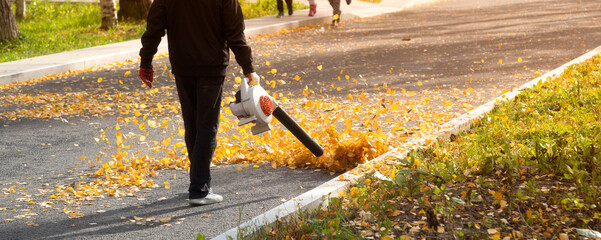 A man, a utility worker, removes leaves from the road with a special device.