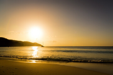 Coral sandy beach in the sunset light. In the distance a sailing yacht.