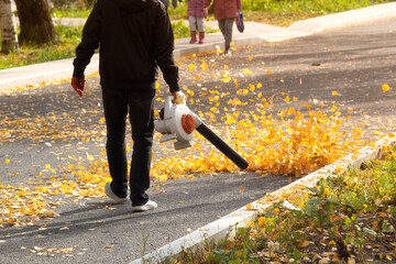 A man, a utility worker, removes leaves from the road with a special device.