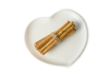 Grissini sticks on a white plate in the shape of a heart. On white background.