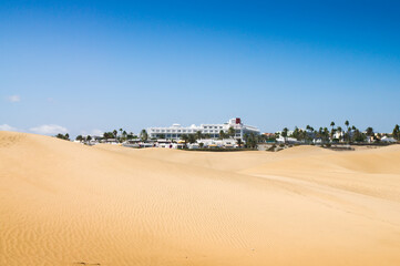 Sand dunes in sunny day. Beautiful white hotel in the background.