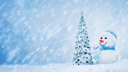 Smiling, happy toy snowman with toy christmas tree and falling snow. Merry Christmas and Happy New Year greeting card with copy-space
