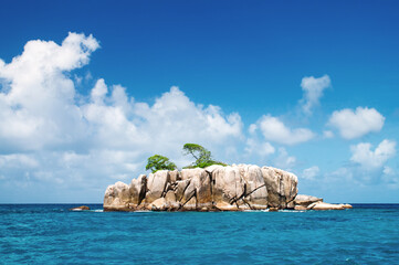 Deserted rocky island in the ocean. Covered with sparse vegetation and trees. The Seychelles.