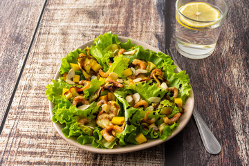 Delicious light dinner, lettuce with fried slices of zucchini, mango and shrimp and almond petals, water with lemon in a glass