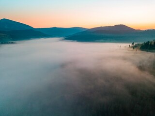 Fototapeta premium Fog spreads over the mountains at dawn. The sun rises on the horizon. Ukrainian Carpathians in the morning. Aerial drone view.