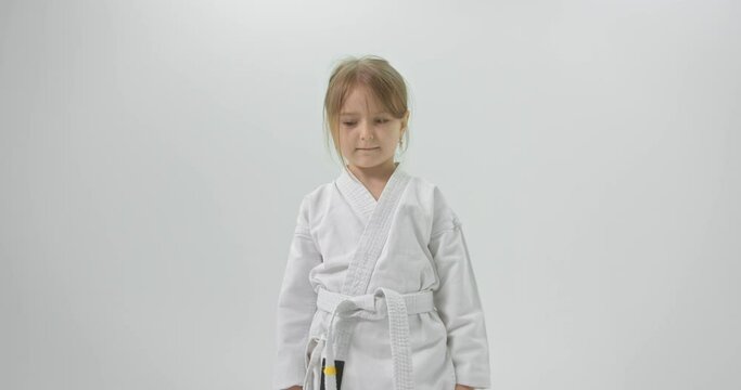 The child is welcomed in karate. The girl in a kimono and on a white background looks at the camera and is greeted.