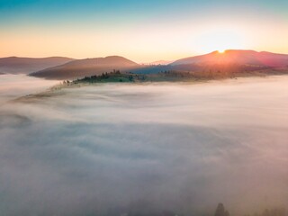 Fog spreads over the mountains at dawn. The sun rises on the horizon. Ukrainian Carpathians in the morning. Aerial drone view.