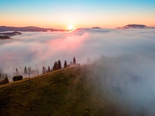 Fog spreads over the mountains at dawn. The sun rises on the horizon. Ukrainian Carpathians in the morning. Aerial drone view.