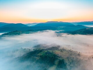 Fog spreads over the mountains at dawn. The sun rises on the horizon. Ukrainian Carpathians in the morning. Aerial drone view.