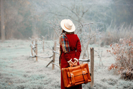 Woman in red coat, and hat with suitcase at snow countryside