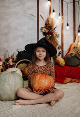 a little girl in a black hat is sitting on a knitted blanket with pumpkins