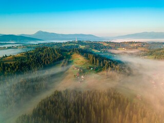 Obraz premium A thin layer of fog floats across the ridge at dawn. Fir trees grow on the slope. Ukrainian Carpathians in the morning. Aerial drone view.