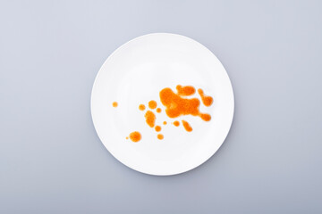 White ceramic plate with leftover food, drops, blots of sauce on a dish surface. Top view, on grey surface