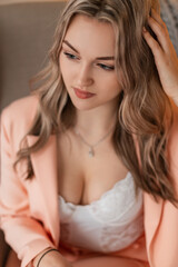 Obraz na płótnie Canvas Beautiful sensual young girl with hair in a fashionable blazer and lacy white lingerie bodysuit with lush breasts sits in a chair