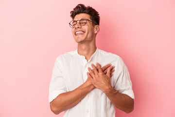 Young caucasian man isolated on pink background has friendly expression, pressing palm to chest. Love concept.
