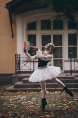 Ballerina posing in autumn park with red book